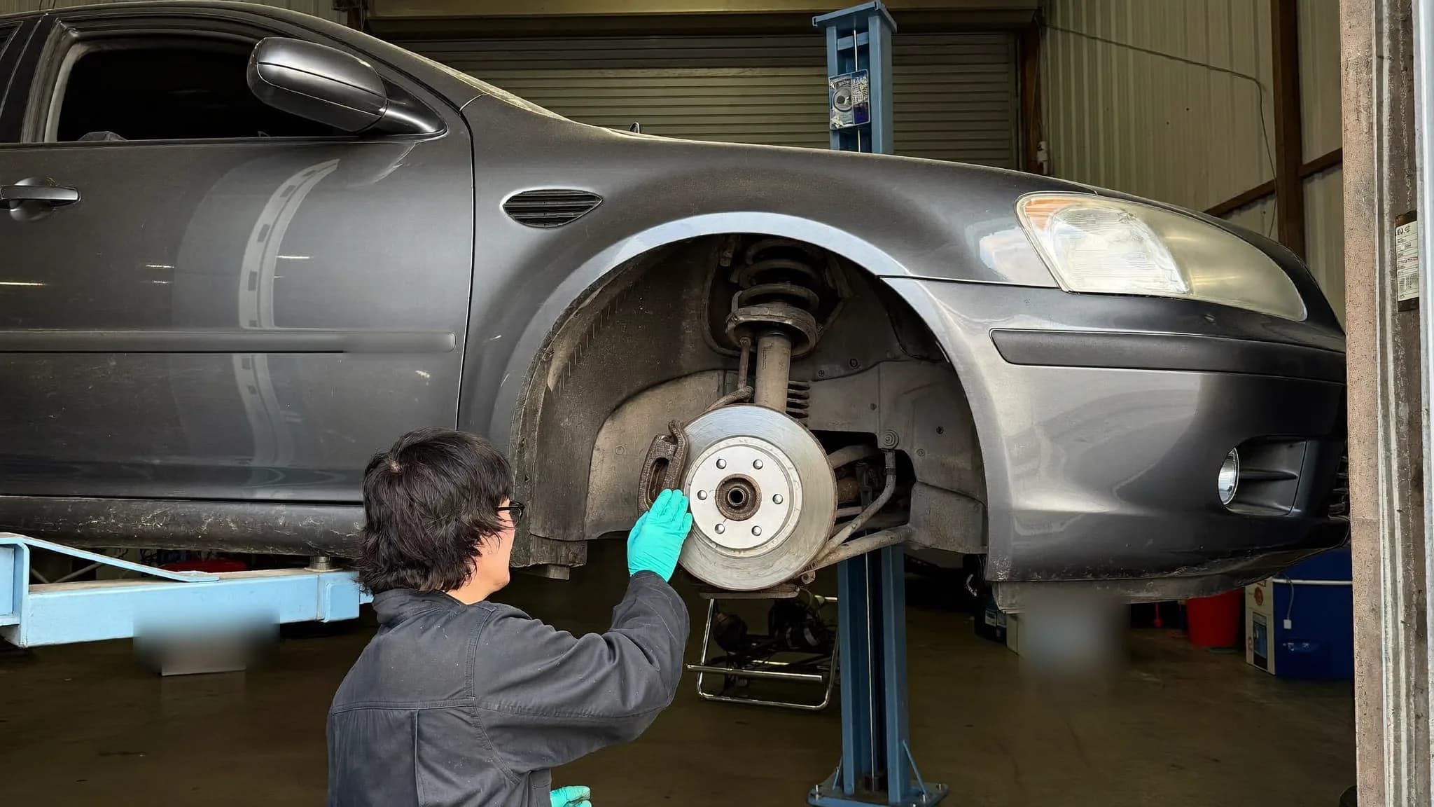 Illustration of a technician inspecting a car's front brake rotor with the wheel removed in a repair shop bay